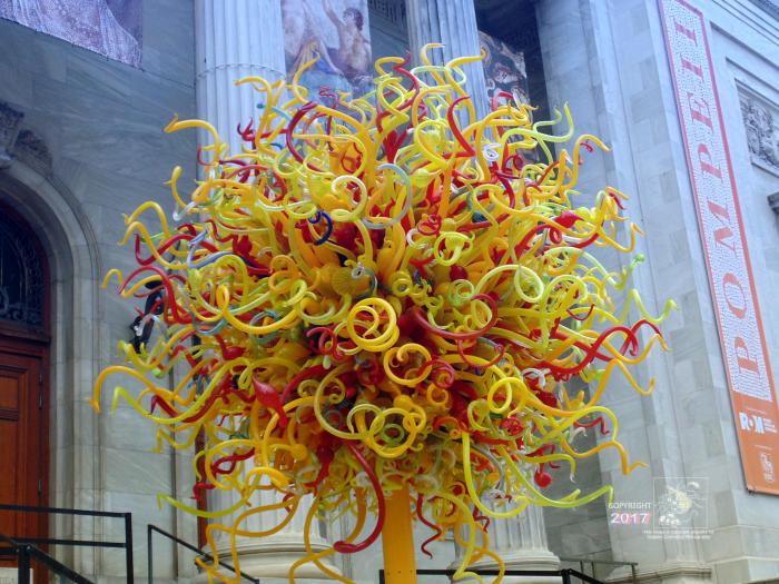  Multi-colored maze ball of plastic tubes attached to yellow metal pole on grey metal stand near Montreal Museum of Fine Arts.